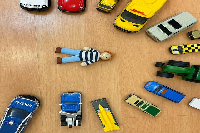 Toy figure surrounded by toy cars arranged in a circle on a wooden floor